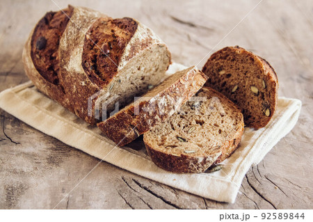 Brown fresh bread with seeds are cut into pieces on old wood background. Top view, copy space 92589844