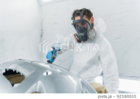 Auto painter varnishing a car body part in a painting booth. Repairman restores vehicle body parts 92590035