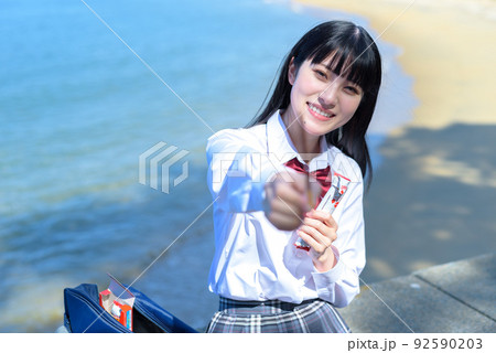 棒状のチョコレートのお菓子を綺麗な海辺の防波堤に座って食べさせる女子高校生 放課後デート 波打ち際 棒状のチョコレートのお菓子を綺麗な海辺の防波堤に座って食べさせる女子高校生 放課後デート 波打ち際 92590203