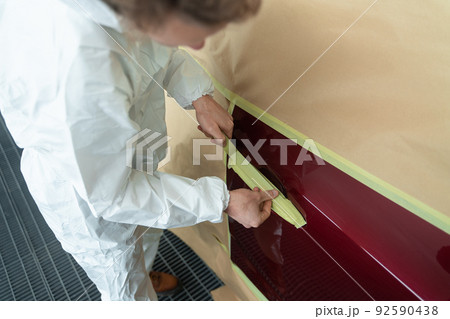 Close-up view of auto painter's who masking a car body before painting with masking tape and paper Close-up view of auto painter's who masking a car body before painting with masking tape and paper 92590438