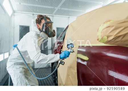 Auto painter in a protective suit and mask sprays a degreaser or other cleaner on a car door using a spray gun. Preparation of vehicle body elements for local repair 92590589