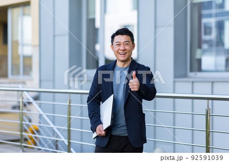 portrait handsome Asian man a university college teacher, businessman, scientist or educator. Standing background modern office center or campus with arms crossed Outside, outdoors looking at camera portrait handsome Asian man a university college teacher, businessman, scientist or educator. Standing background modern office center or campus with arms crossed Outside, outdoors looking at camera 92591039