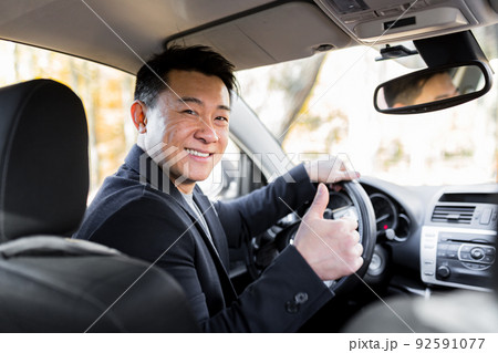 A man driving an Asian car behind the wheel looks at the camera and smiles 92591077