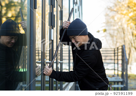 Asian man robber tries to break the door lock with a large metal crowbar tool 92591199