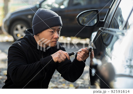 Male asian thief steals car breaks door lock with mechanical screwdriver tool Male asian thief steals car breaks door lock with mechanical screwdriver tool 92591614