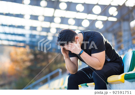 Frustrated Asian male athlete depressed, dissatisfied with the result of his training, in despair after running, resting sitting 92591751