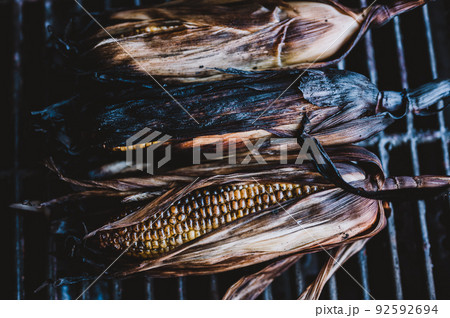 slightly charred sweet corn on the cob with husk on resting on a grill grate 92592694