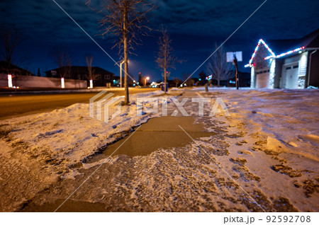 Ice and snow on a sidewalk at night with streetlight reflecting off the slick surface. Ice and snow on a sidewalk at night with streetlight reflecting off the slick surface. 92592708