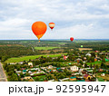 Large beautiful hot balloons fly high in the sky over scenery green field and forest. Extreme entertainment for vacation and leisure 92595947