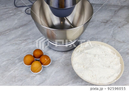 Modern kitchen machine and ingredients for preparing dough (eggs and flour) on a kitchen table 92596055