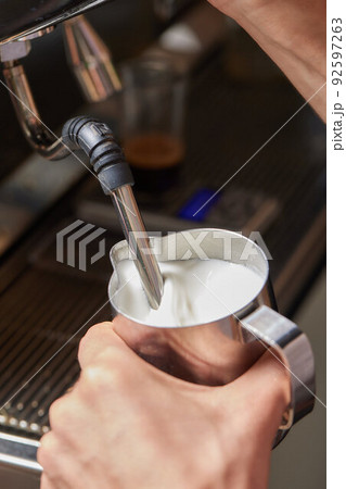 Top view shot of professional barista pouring milk from jar in to a cup of coffee, coffee being prepared by a barista. Focus on hands holding cup of coffee. 92597263