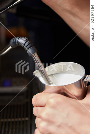 Top view shot of professional barista pouring milk from jar in to a cup of coffee, coffee being prepared by a barista. Focus on hands holding cup of coffee. Top view shot of professional barista pouring milk from jar in to a cup of coffee, coffee being prepared by a barista. Focus on hands holding cup of coffee. 92597264