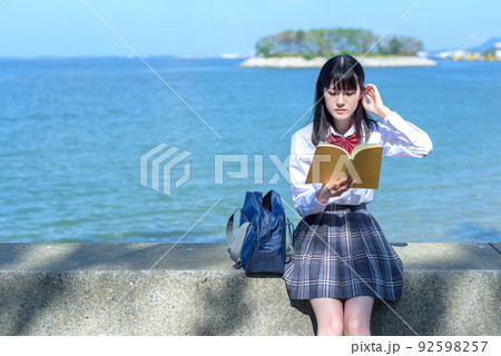 綺麗な海辺の防波堤に座って本を読む女子高校生 読書 勉強 小説 放課後