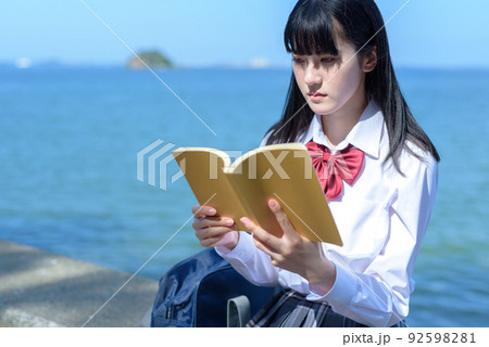 綺麗な海辺の防波堤に座って本を読む女子高校生　読書　勉強　小説　放課後　波打ち際 92598281