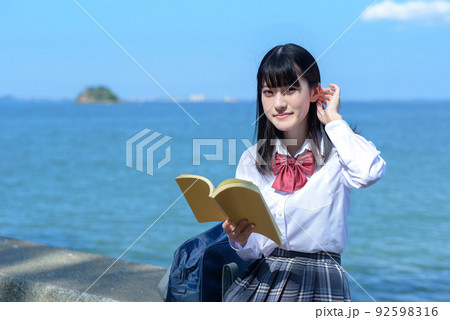 綺麗な海辺の防波堤に座って本を読む女子高校生　読書　勉強　小説　放課後　波打ち際 92598316