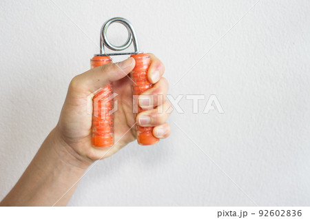 Cropped shot view of woman left hand handle a hand grip for exercise with white wall background. Cropped shot view of woman left hand handle a hand grip for exercise with white wall background. 92602836