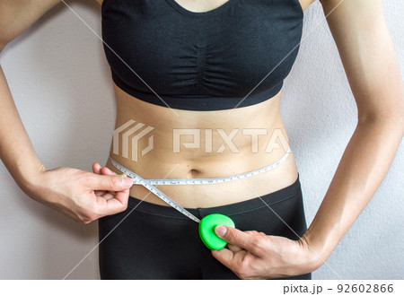 Sportswoman measuring her waist by measure tape after hard workout isolated on white wall background. Sportswoman measuring her waist by measure tape after hard workout isolated on white wall background. 92602866