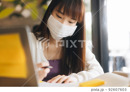 Young adult asian female with protective face mask work and study at cafe new normal lifestyle. Young adult asian female with protective face mask work and study at cafe new normal lifestyle. 92607603