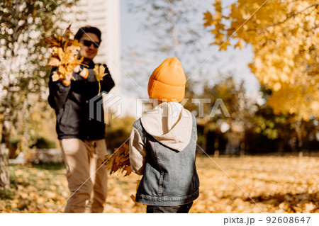 Father and son having fun in autumn park with fallen leaves, throwing up leaf. Child kid boy and his dad outdoors playing with maple leaves. 92608647
