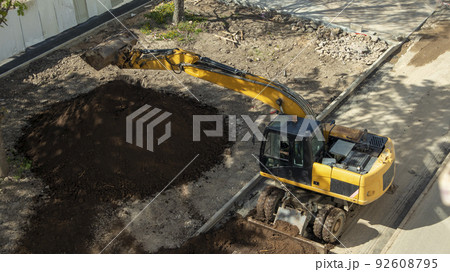 yellow construction excavator throws the earth onto a flower bed, an unusual angle yellow construction excavator throws the earth onto a flower bed, an unusual angle 92608795
