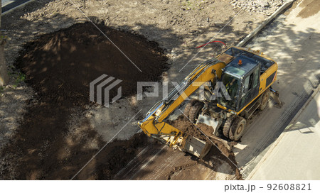 yellow construction excavator throws the earth onto a flower bed, an unusual angle 92608821