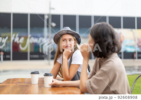 Pretty young girl wearing hat drinking coffee with her friend 92608908