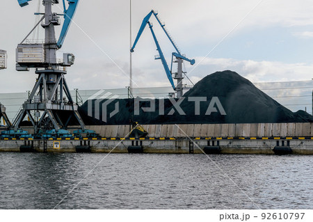 Cargo cranes in the port coal terminal. Pile of coal on the pier. 92610797
