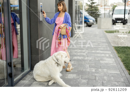 Young stylish woman getting access to the building by attaching smartphone to intercom 92611209