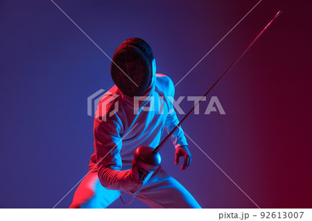 Male fencer with smallsword practicing fencing isolated on purple background in neon light. Sport, energy, skills, achievements Male fencer with smallsword practicing fencing isolated on purple background in neon light. Sport, energy, skills, achievements 92613007