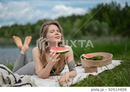 Girl relaxing and eat watermelon outdoor near lake. Picnic in nature Girl relaxing and eat watermelon outdoor near lake. Picnic in nature 92614806