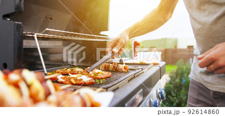 Young man grilling some kind of meats on the gas grill during lovely summer time, food concept 92614860