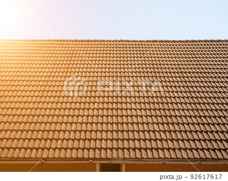 Red tiled roof. Side view. The roof of the house with a brand new red tiled masonry against the sky in the rays of the sun. Soft focus. Red tiled roof. Side view. The roof of the house with a brand new red tiled masonry against the sky in the rays of the sun. Soft focus. 92617617
