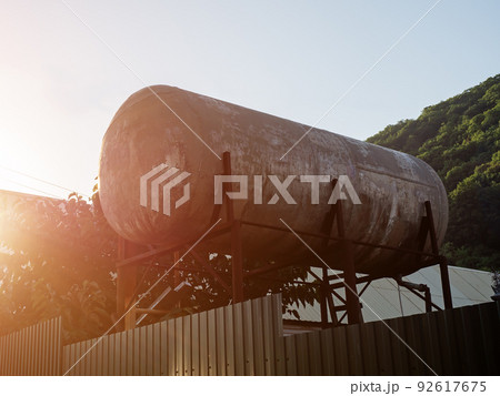 Large iron water tank behind the fence. A large water tank on rusty iron supports stands in a private yard. Solar water heater on props. Alternative energy and ecology 92617675
