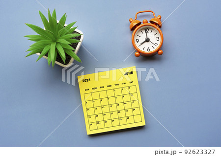 June 2023 calendar on adhesive note with alarm clock set at 8 o'clock. 92623327