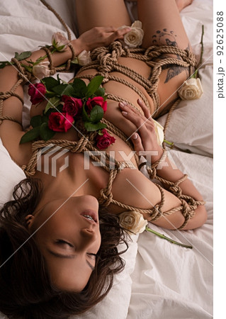 Sensual naked woman tied with ropes lying on bed 92625088