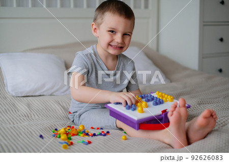 Little happy caucasian boy in a light room on the bed collects color mosaic to creating images 92626083