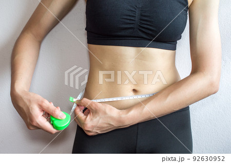 Sportswoman measuring her waist by measure tape after hard workout isolated on white wall background. 92630952