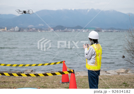 工事現場でドローンを操縦して写真撮影をする若い女性作業員 92634182