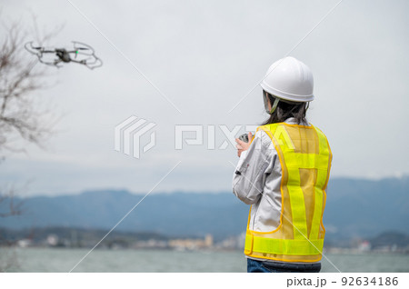 工事現場でドローンを操縦して写真撮影をする若い女性作業員 92634186