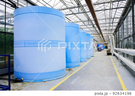 Electric motor water pump at greenhouse. Interior and equipment with pipelines and water tank in modern greenhouse. Modern greenhouse equipment for drip irrigation. Plant growth liquid tanks. 92634196