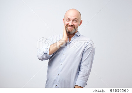 Pleasant charming european male with beard bring hands towardfacewith lovely expression as if receiving compliment Pleasant charming european male with beard bring hands towardfacewith lovely expression as if receiving compliment 92636569