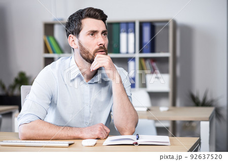 Close up photo. Upset, tired and thoughtful young man, office worker, manager, freelancer. He holds his head in his hands. Sitting at a computer desk in the office Close up photo. Upset, tired and thoughtful young man, office worker, manager, freelancer. He holds his head in his hands. Sitting at a computer desk in the office 92637520