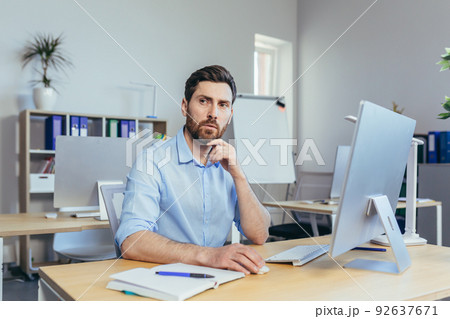 Portrait of a serious and focused businessman, a man working in a bright office during the day, at the computer looking at the monitor, in casual clothes 92637671
