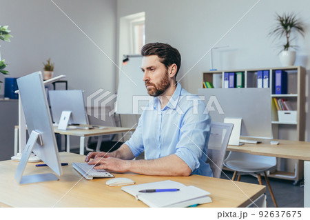 Thinking business man, working in a modern office during the day, sitting at a table, working with a computer, thinking about solving a business contract 92637675