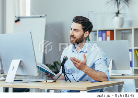 Successful and happy business coach mentor, records audio podcast, uses professional microphone, businessman in modern white office, conducts online business training 92638248