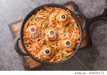 Scary Halloween food of meatballs with monster eyes and pasta with tomato sauce in a pan on the table close-up. Horizontal top view Scary Halloween food of meatballs with monster eyes and pasta with tomato sauce in a pan on the table close-up. Horizontal top view 92640172