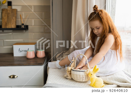 Little girl collects  Easter basket sitting on the windowsill at home 92640610