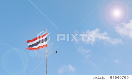 The Thai flag has red white and blue colors on the fabric. On the high pole, the wind blew the flag. sunlight shining clear sky A small bird flew by. There are beautiful bright clouds 92640799