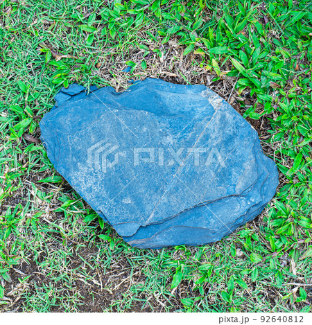 An old rough stone slab laid out on a green lawn as a plaque for an outdoor photo shoot. 92640812