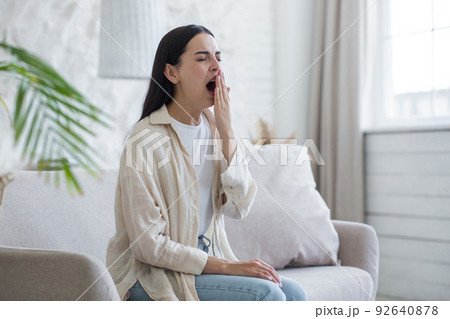 Beautiful woman at home sitting on the sofa tired yawning, sleepless brunette 92640878